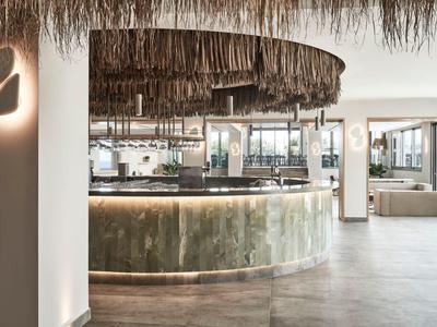 Moderner Hotelbarbereich mit rundem Tresen und natürlichem, strohgedecktem Deckenakzent.