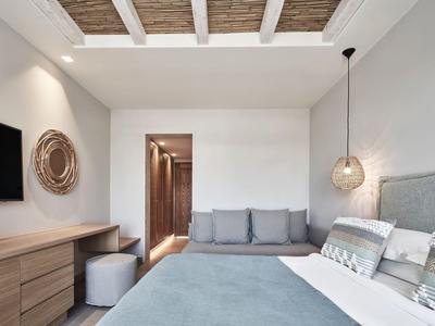 Nowoczesny pokój hotelowy z podwójnym łóżkiem, szarą sofą i minimalistyczną drewnianą komodą.