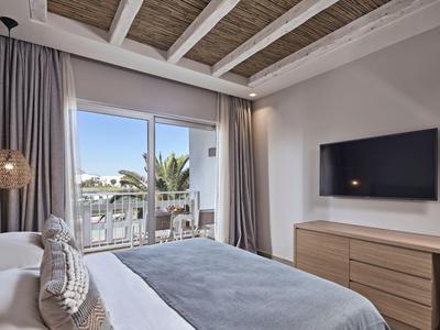 Nowoczesny pokój hotelowy z łóżkiem podwójnym, drewnianymi meblami i balkonem z widokiem na palmy.