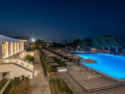 Beleuchteter Hotelpool mit Liegen und Sonnenschirmen bei Nacht unter klarem Himmel.