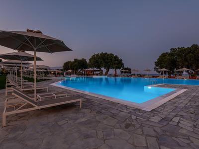 Abendaufnahme eines beleuchteten Pools mit Liegestühlen und Sonnenschirmen im Freien.