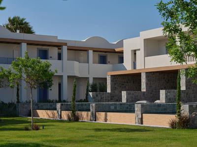Modernes Hotelgebäude mit weißen Wänden, Balkonen und gepflegtem Grünbereich bei klarem Himmel.