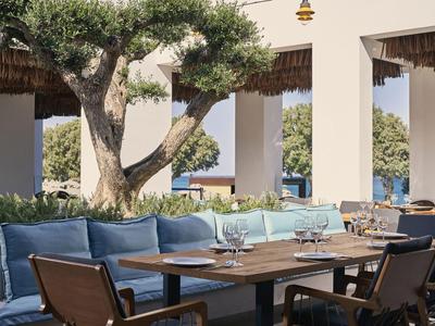 Moderner Außenbereich eines Hotels mit Holztisch, Stühlen und blauen Kissen unter einem überdachten Bereich.