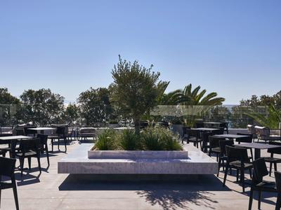 Moderne Hotelterrasse mit Tischen, Stühlen und bepflanztem Sitzbereich bei klarem Himmel.