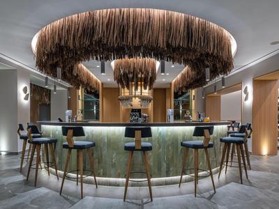 Moderner Hotelbarbereich mit runden Tresen, Holzstühlen und auffälliger Kronleuchterdecke.