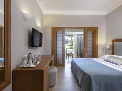 Modernes Hotelzimmer mit Doppelbett, Fernseher und Blick auf Balkon mit Garten.