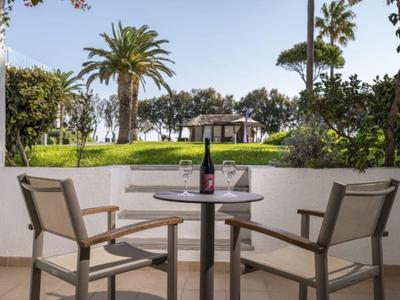Terrasse mit Tisch, zwei Stühlen, Weinflasche und Gläsern mit Blick auf Palmen und Garten.