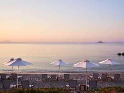 Strand mit Liegestühlen und Sonnenschirmen am ruhigen Meer bei Sonnenuntergang.