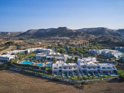 Hotelanlage mit Pool und weißen Gebäuden in einer hügeligen Landschaft bei klarem Himmel.