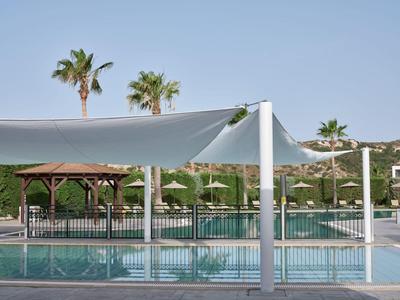 Moderner Poolbereich mit Segeltuchsonnenschutz, Palmen und grüner Umgebung bei klarem Himmel