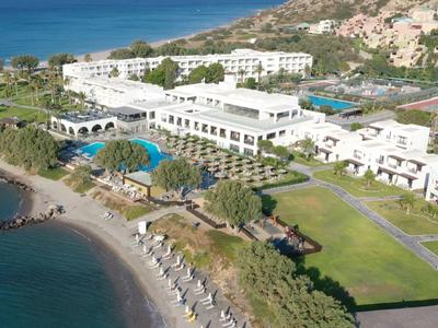 Blick auf ein großes Resort am Meer mit Pool und Strandanlage neben Felsen und grüner Wiese.