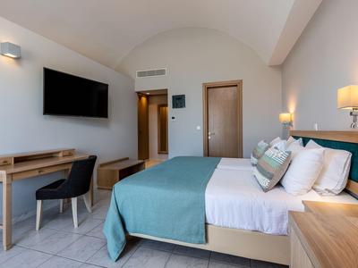 Modernes Hotelzimmer mit Doppelbett, Schreibtisch und Fernseher, in hellen Farben eingerichtet.