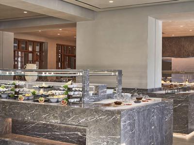 Modernes Hotelrestaurant mit Buffetstationen aus grauem Marmor und verschiedenen Speisen.