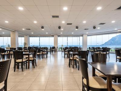 Grande sala da pranzo con molti tavoli e sedie e vista sulle montagne attraverso grandi finestre.