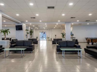 Hall dell'hotel luminoso con divani neri, tavolini in vetro e piante decorative.