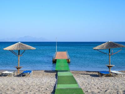 Spiaggia sabbiosa con due ombrelloni di paglia e un molo verde che si estende nel mare blu.