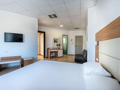 Camera d'hotel moderna con ampio letto, TV, tavolo e sedia in un design luminoso e semplice.