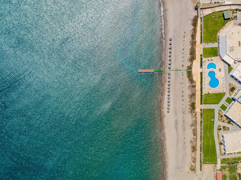 Linea costiera con mare blu chiaro, spiaggia sabbiosa e edifici adiacenti con piscine