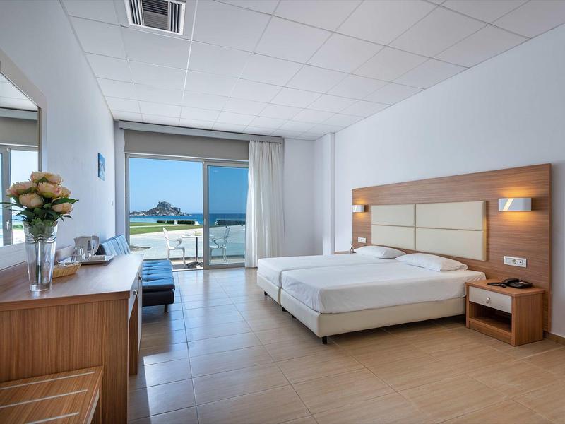 Camera d'hotel luminosa con letto matrimoniale, scrivania, TV e vista sul mare attraverso grandi finestre.