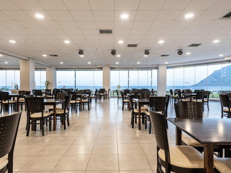 Grande sala da pranzo con molti tavoli e sedie e vista sulle montagne attraverso grandi finestre.