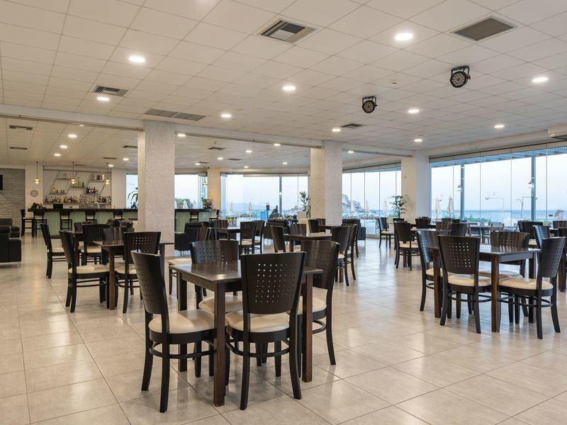 Area ristorante luminosa con tavoli e sedie di legno vicino a grandi finestre.