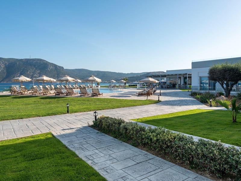 Area dell'hotel con prati curati e vista sulla spiaggia e le montagne sotto un cielo sereno.