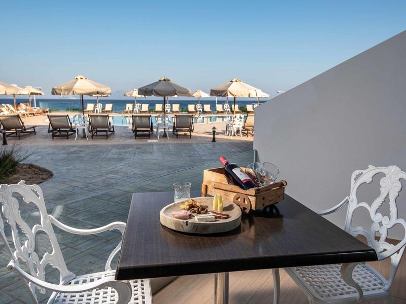 Tavolo con snack e bevande su terrazza con sedie bianche e vista mare.