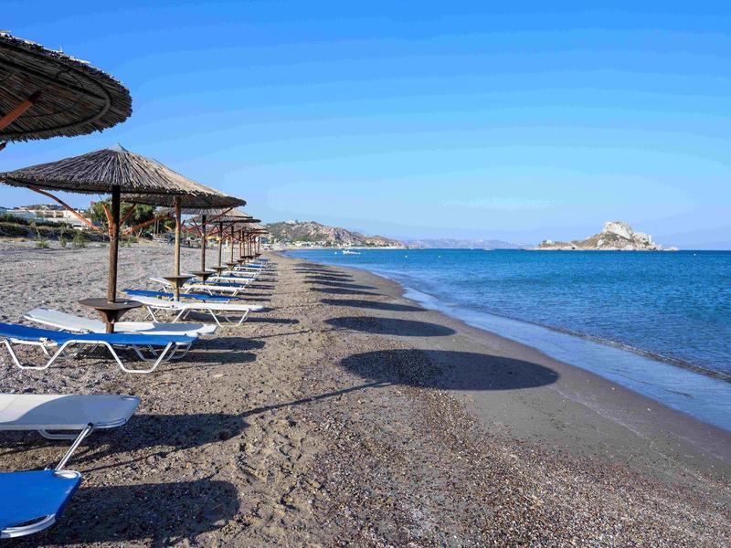 Spiaggia vuota con lettini e ombrelloni sul mare calmo e blu sotto un cielo sereno.