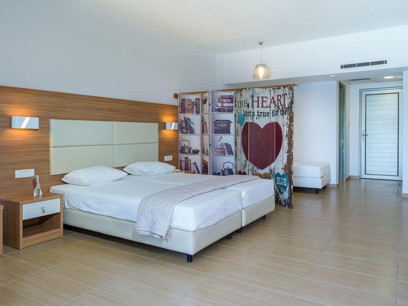 Camera d'hotel luminosa con letto matrimoniale, comodini, paravento decorativo e pavimento in legno.