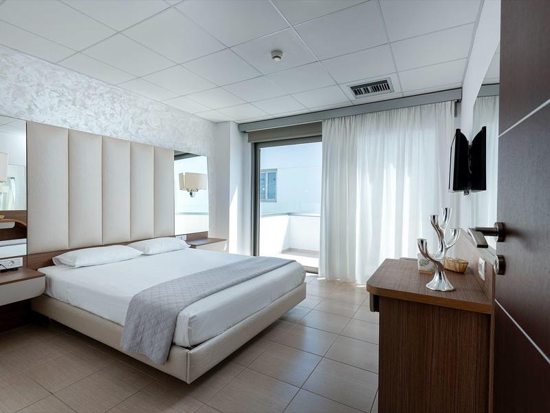 Camera d'hotel moderna con letto matrimoniale, scrivania, TV e accesso al balcone con vista.