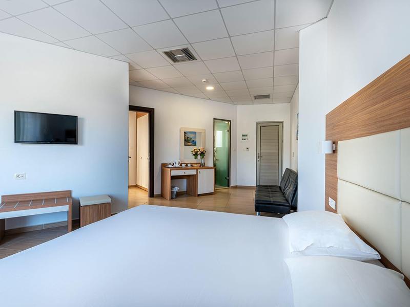 Camera d'hotel moderna con ampio letto, TV, tavolo e sedia in un design luminoso e semplice.