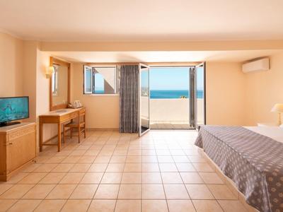 Chambre d'hôtel lumineuse avec lit double, télévision, bureau et balcon avec vue sur la mer.
