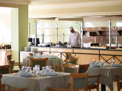 Un restaurant calme avec des tables dressées et un chef dans la cuisine ouverte.