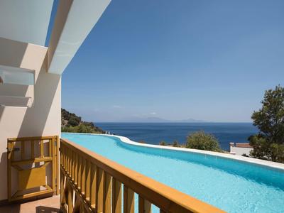 Piscine à débordement avec vue sur la mer et ciel bleu clair à côté d'un bâtiment moderne.