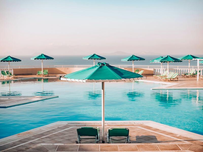 Piscine avec parasols verts et deux chaises longues au bord avec vue sur la mer.