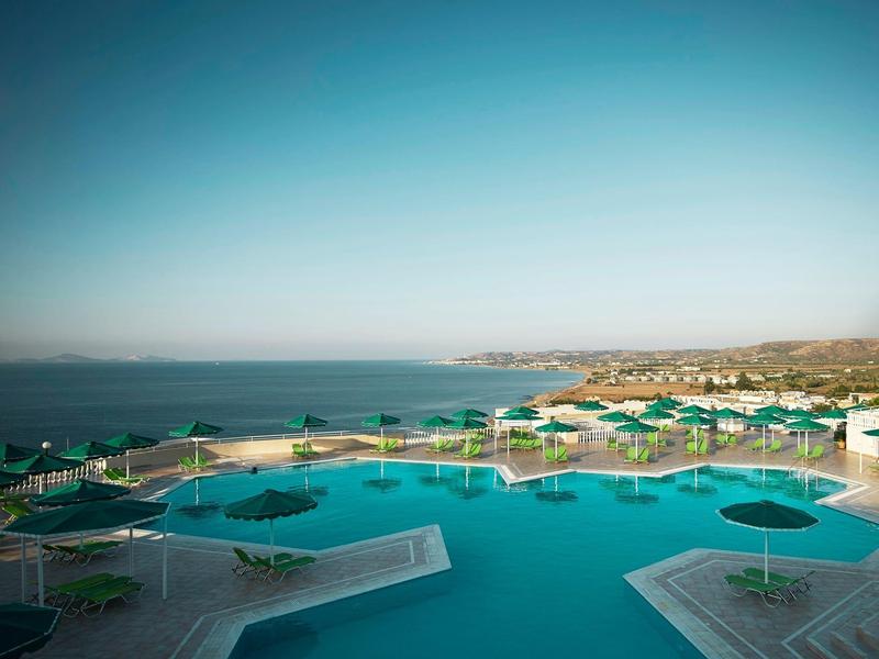 Grand bassin avec parasols verts et vue sur la mer sous un ciel clair.