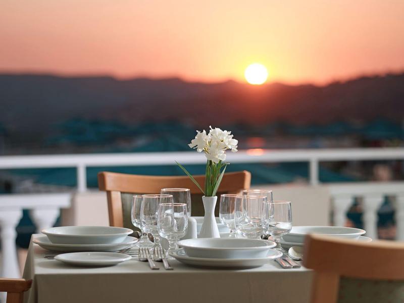 Une table dressée avec vue sur un coucher de soleil sur des collines ondulantes.
