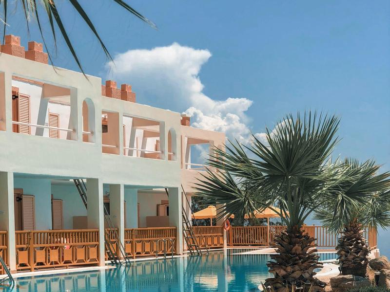 Hôtel avec piscine, rambarde en bois et palmiers sous un ciel clair