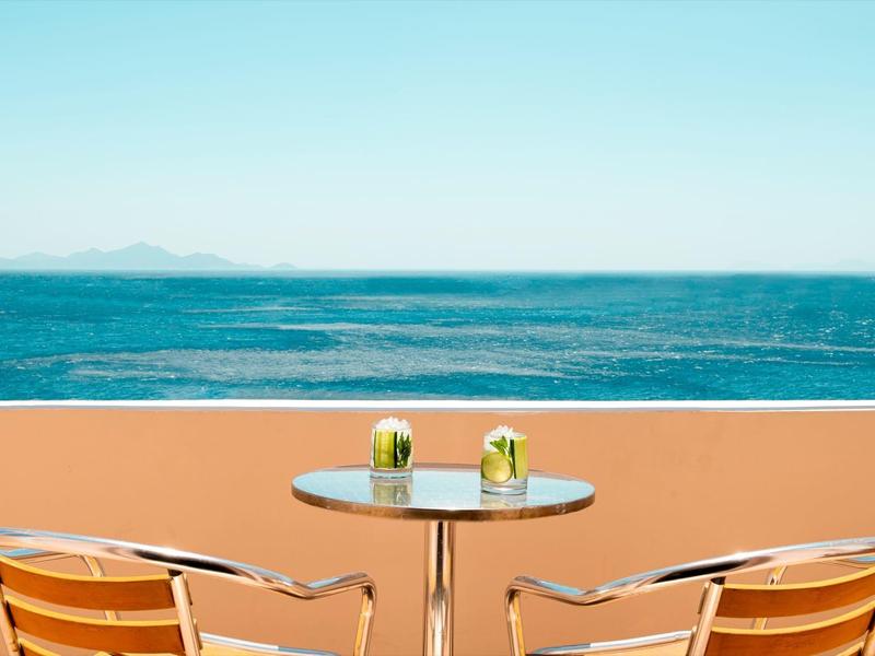 Table de balcon avec deux boissons et vue sur la mer sous un ciel clair.