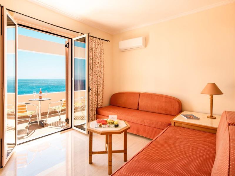 Salon lumineux avec porte terrasse et vue sur la mer, équipé de canapés rouges et d'une petite table.