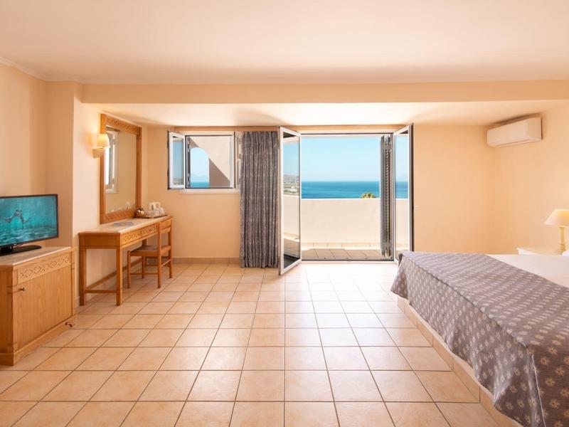 Chambre d'hôtel lumineuse avec lit double, télévision, bureau et balcon avec vue sur la mer.