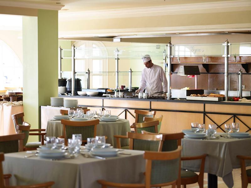 Un restaurant calme avec des tables dressées et un chef dans la cuisine ouverte.