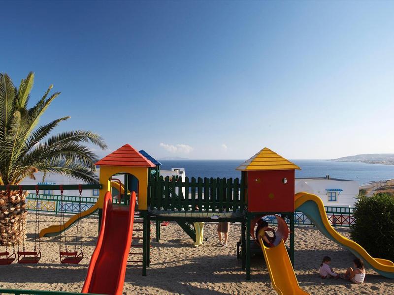 Aire de jeux colorée pour enfants avec toboggans au bord de la mer et palmiers en arrière-plan.