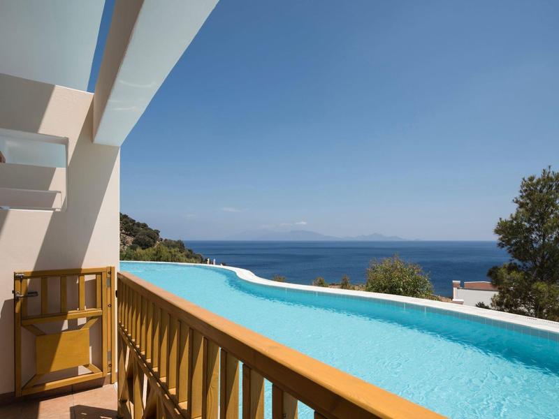Piscine à débordement avec vue sur la mer et ciel bleu clair à côté d'un bâtiment moderne.