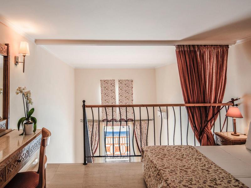 Chambre confortable avec balcon, rideaux rouges et commode en bois dans une chambre d'hôtel.