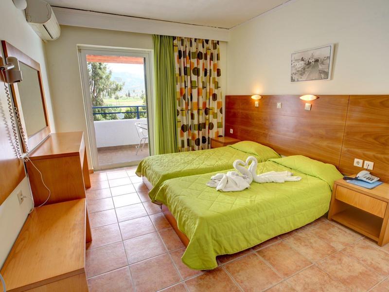 Helles Hotelzimmer mit zwei Betten, grünen Bettdecken, Holzmöbeln und Balkon mit Blick ins Grüne.