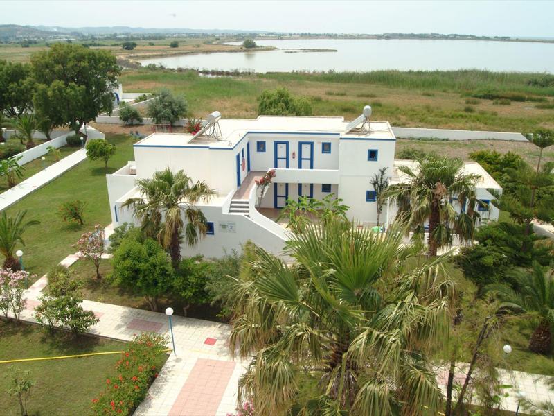 Weißes Gebäude mit blauen Fensterläden, umgeben von Palmen und Grünflächen nahe eines Sees.