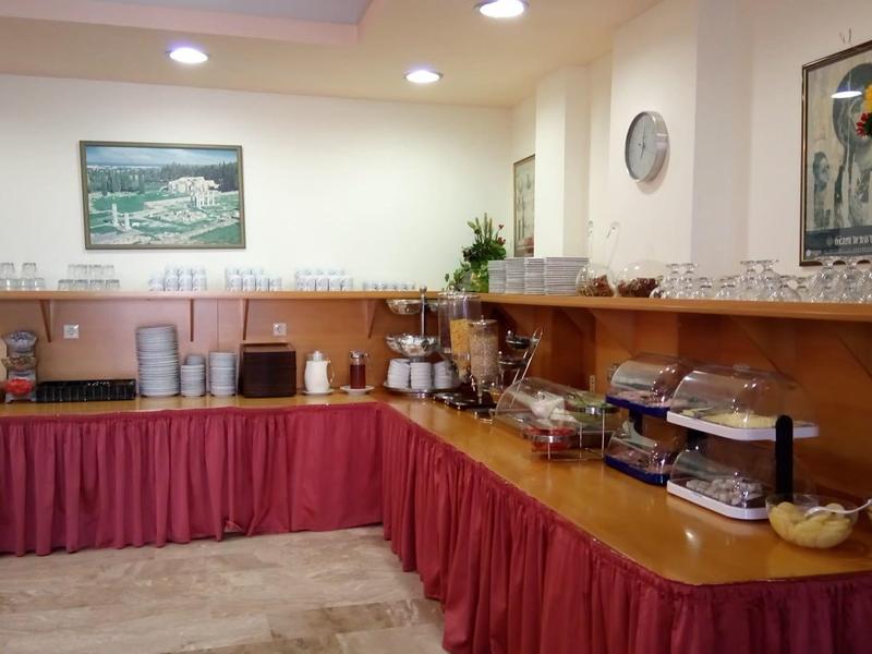 Büffet mit Holzmöbeln, roter Tischdecke, Gläsern, Früchten und Frühstückszubehör in hellem Raum.