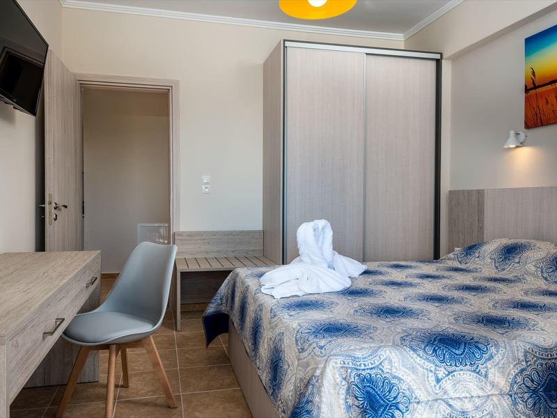 Modern eingerichtetes Schlafzimmer mit blau gemustertem Bett, Schreibtisch, Stuhl und großem Schrank.