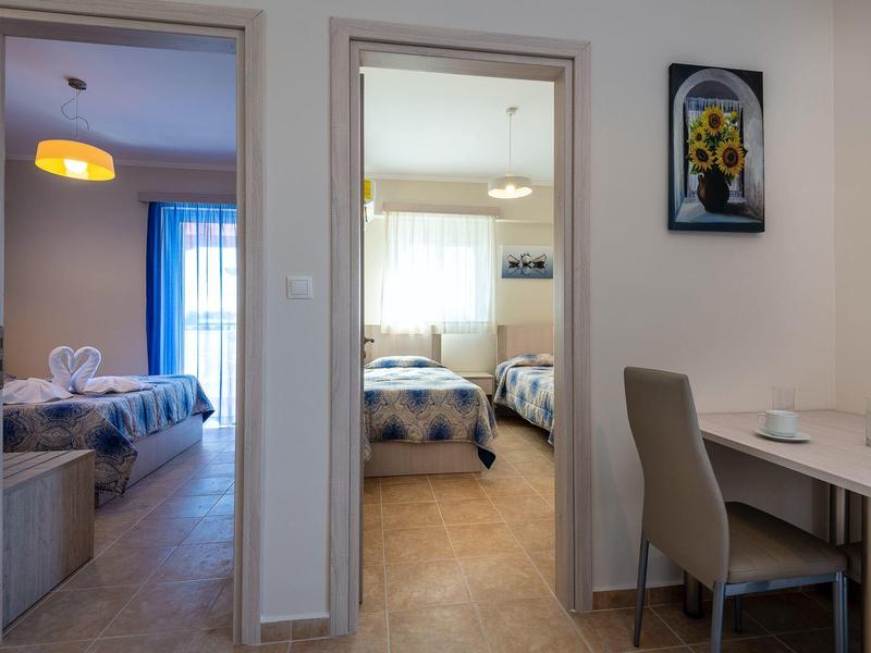 Innenraum mit zwei Schlafzimmern, hellen Vorhängen, modernen Möbeln und schlichtem Esstisch mit Stühlen.